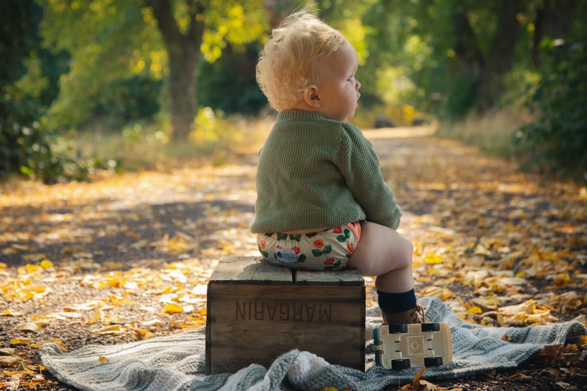 ett barn som sitter på en låda i höstmiljö och har på sig en tygblöja med vallmoblommor
